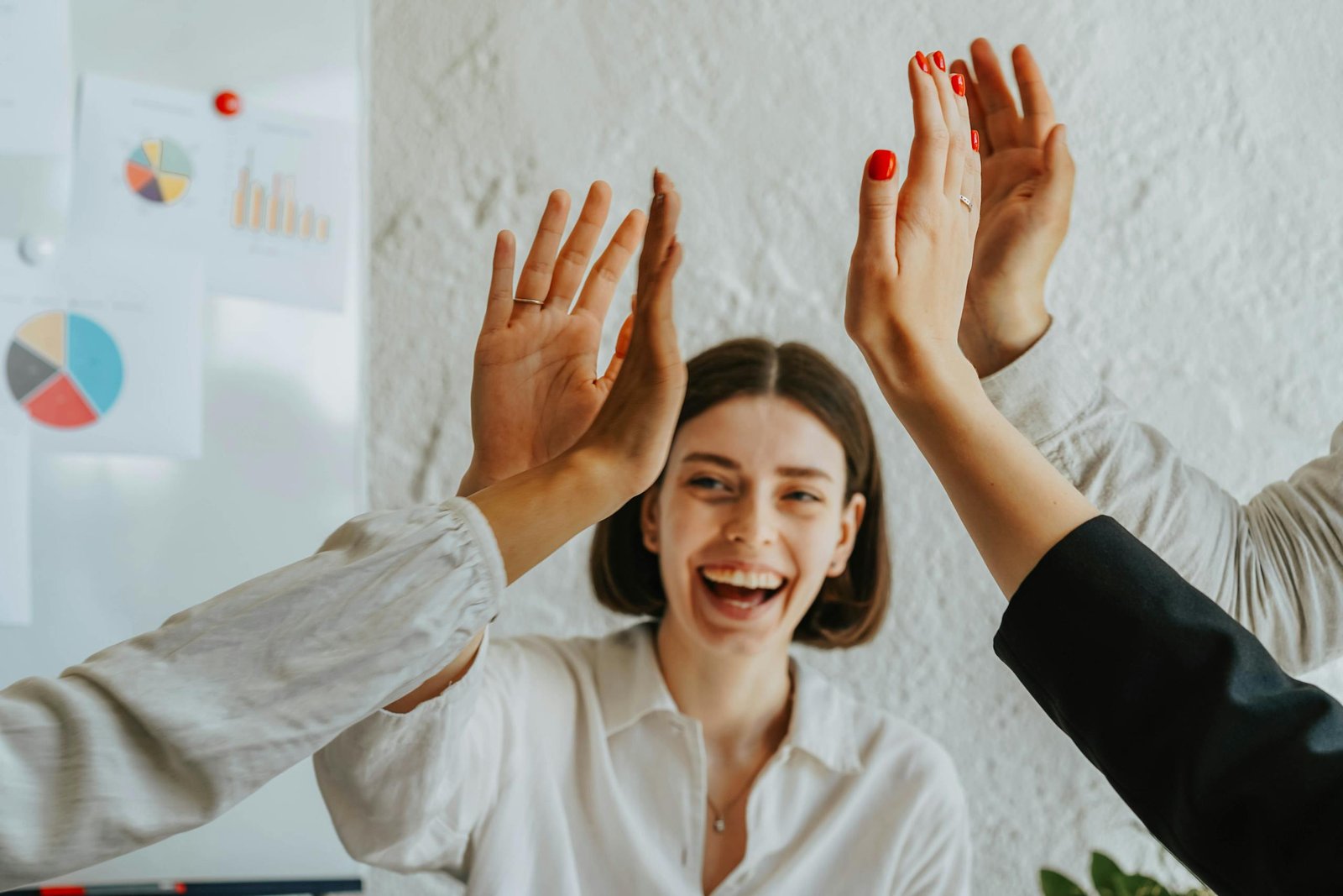 Diverse colleagues share a joyful high five, showcasing teamwork and unity in the office.